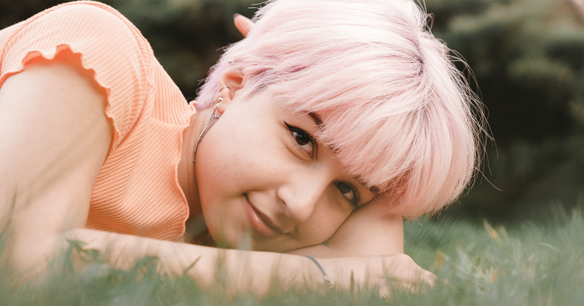 Woman laying in grass smiling, coping with daily anxiety.