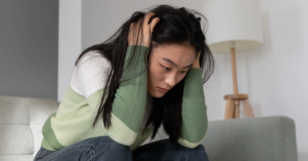 Young woman sitting on a couch holding her head with a distressed, overwhelmed expression