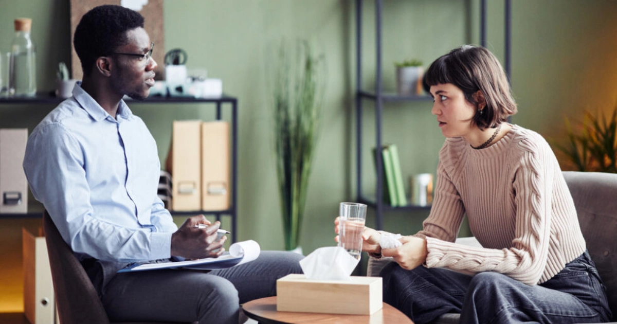 Therapist speaking with a client who holds a glass of water during a counseling session.
