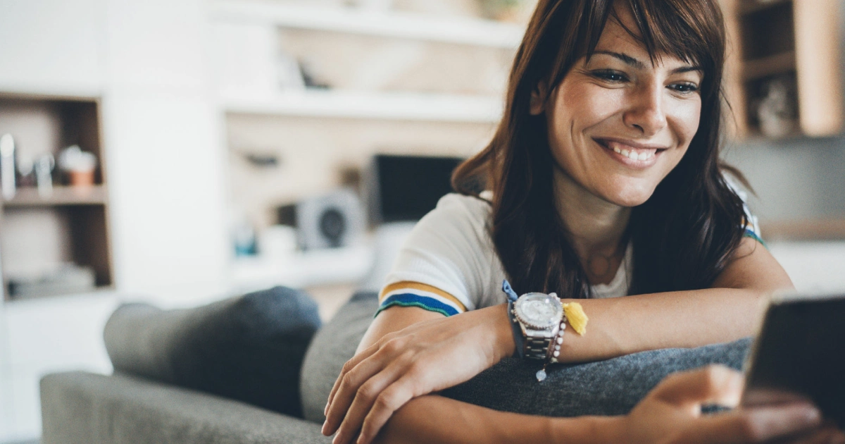 Smiling woman relaxing on a couch while looking at her phone.