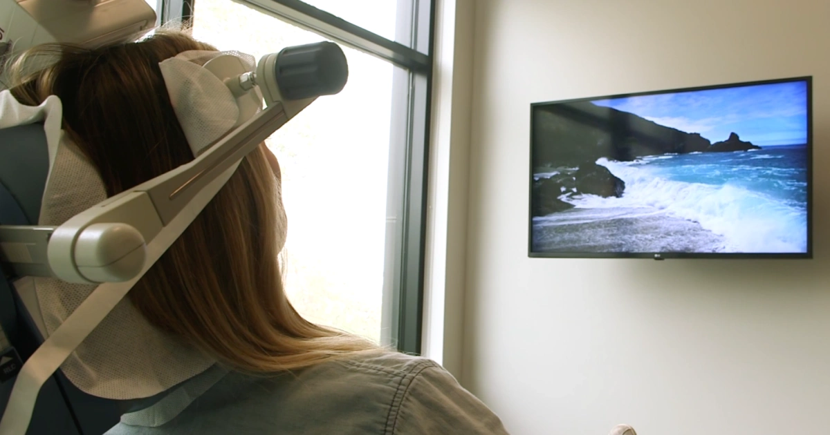 Person receiving TMS treatment while watching a calming ocean scene on a wall-mounted screen