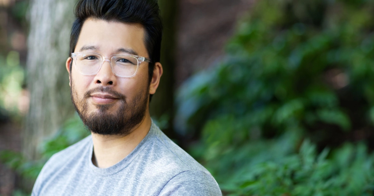 Man with glasses sitting outdoors and looking calmly toward the camera.
