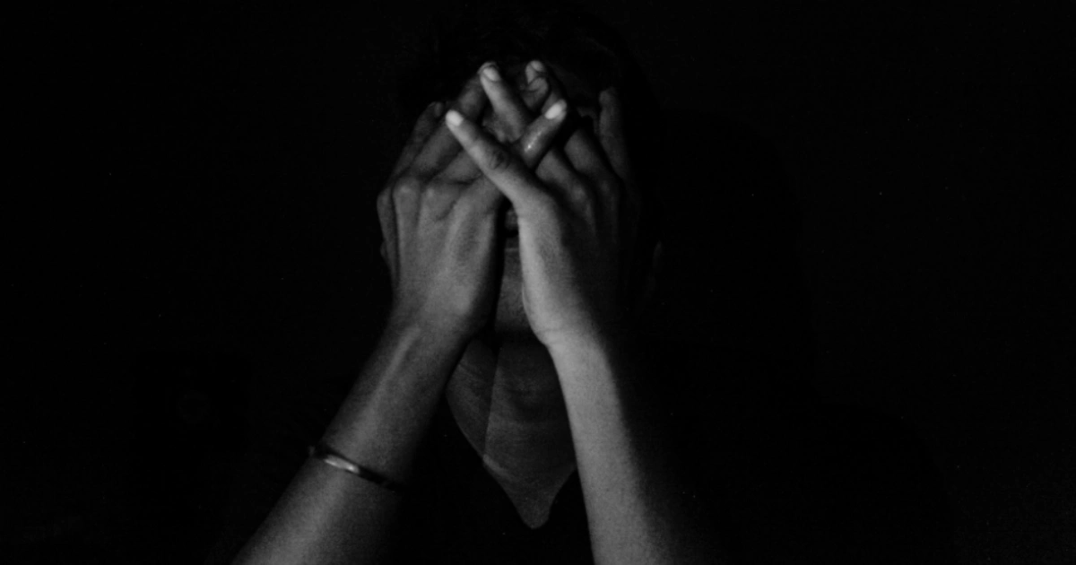 Woman sitting on the floor against a wall with her hands covering her face in distress