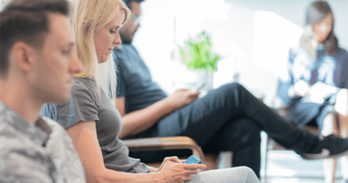 People sitting in a waiting room, focused on their phones or reading.