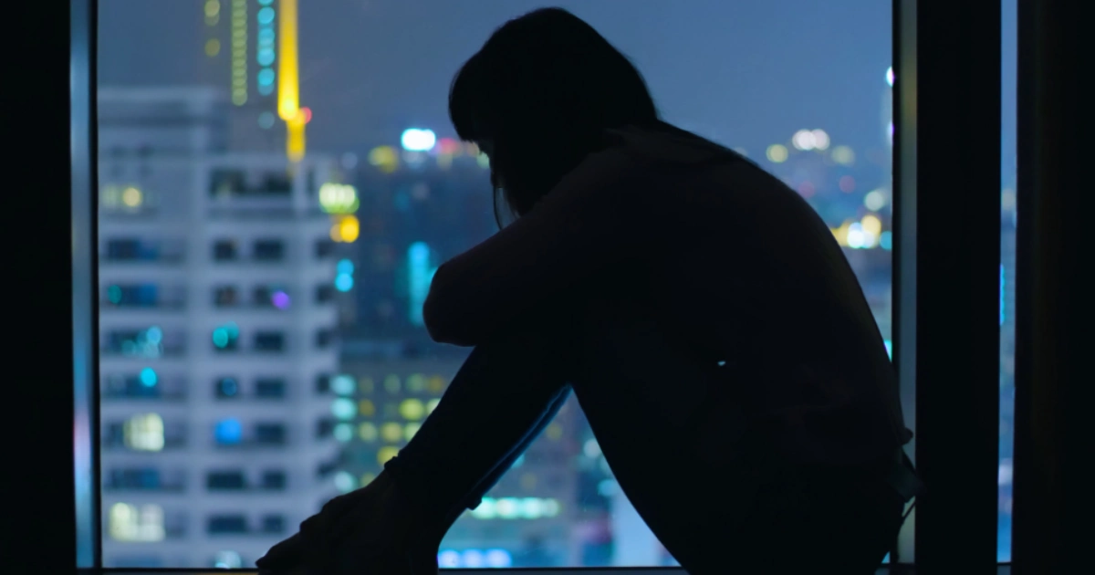 Woman sitting on the floor with her hands over her face in a distressed posture