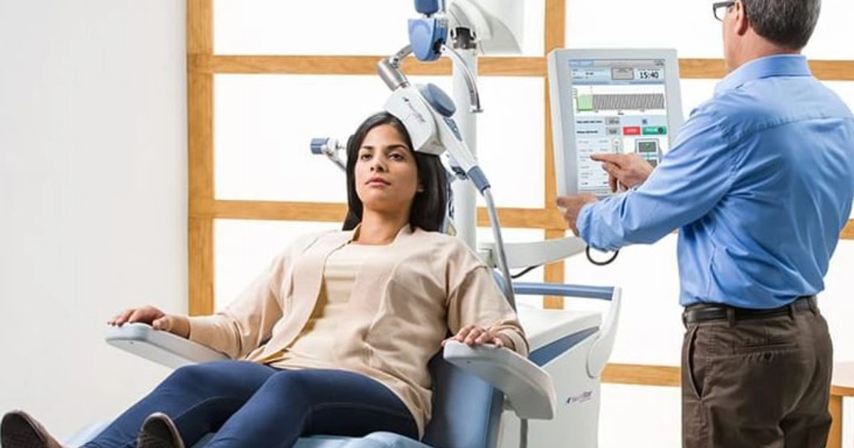 Patient seated in a TMS chair while a clinician operates the treatment device.