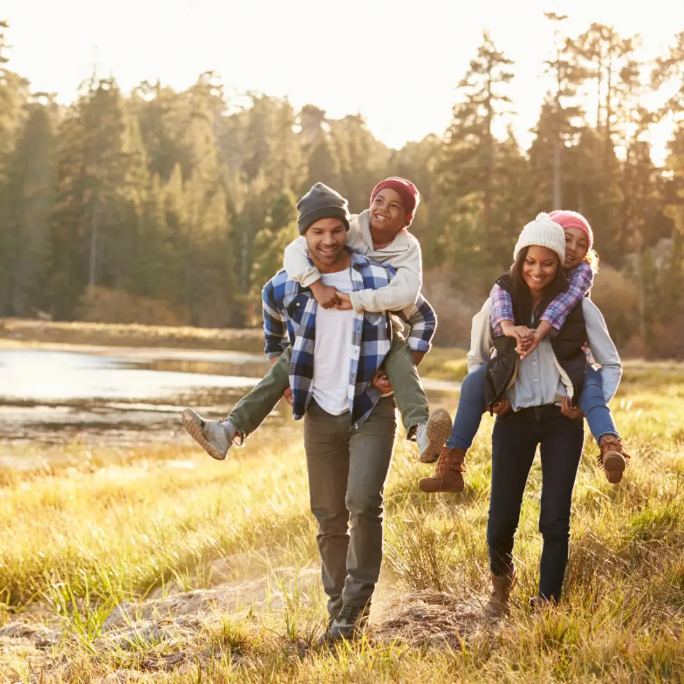 Family walking outdoors with parents giving piggyback rides to their smiling children