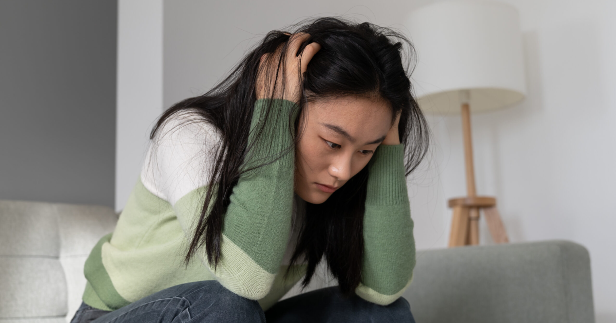 Young woman sitting on a couch holding her head with a stressed, overwhelmed expression